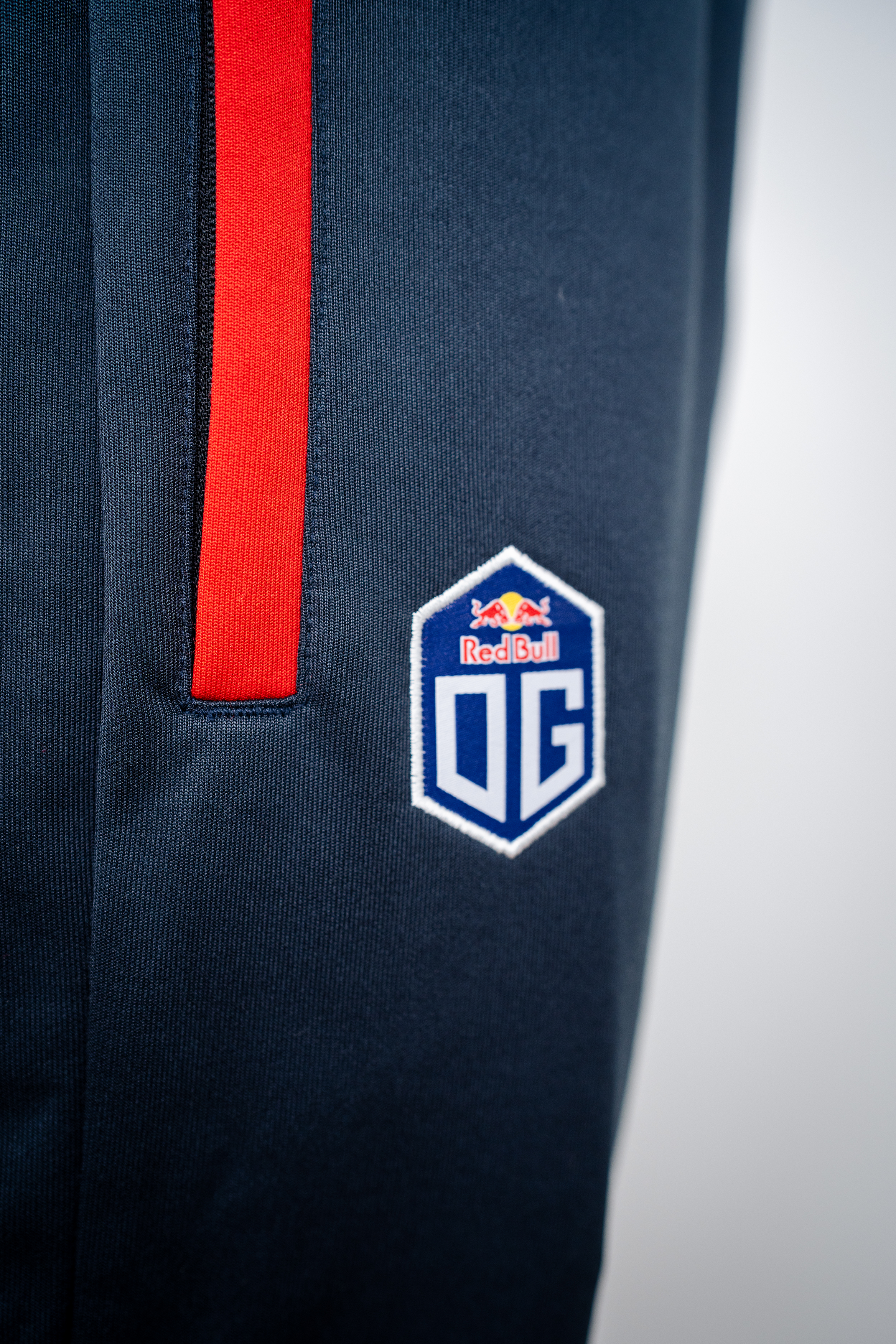 Dark grey athletic pants customized for Esports Team OG, featuring a tapered fit with an elastic waistband and drawstrings. The pants display the OG team logo on the left thigh and include subtle seam details along the sides, shown against a white background.