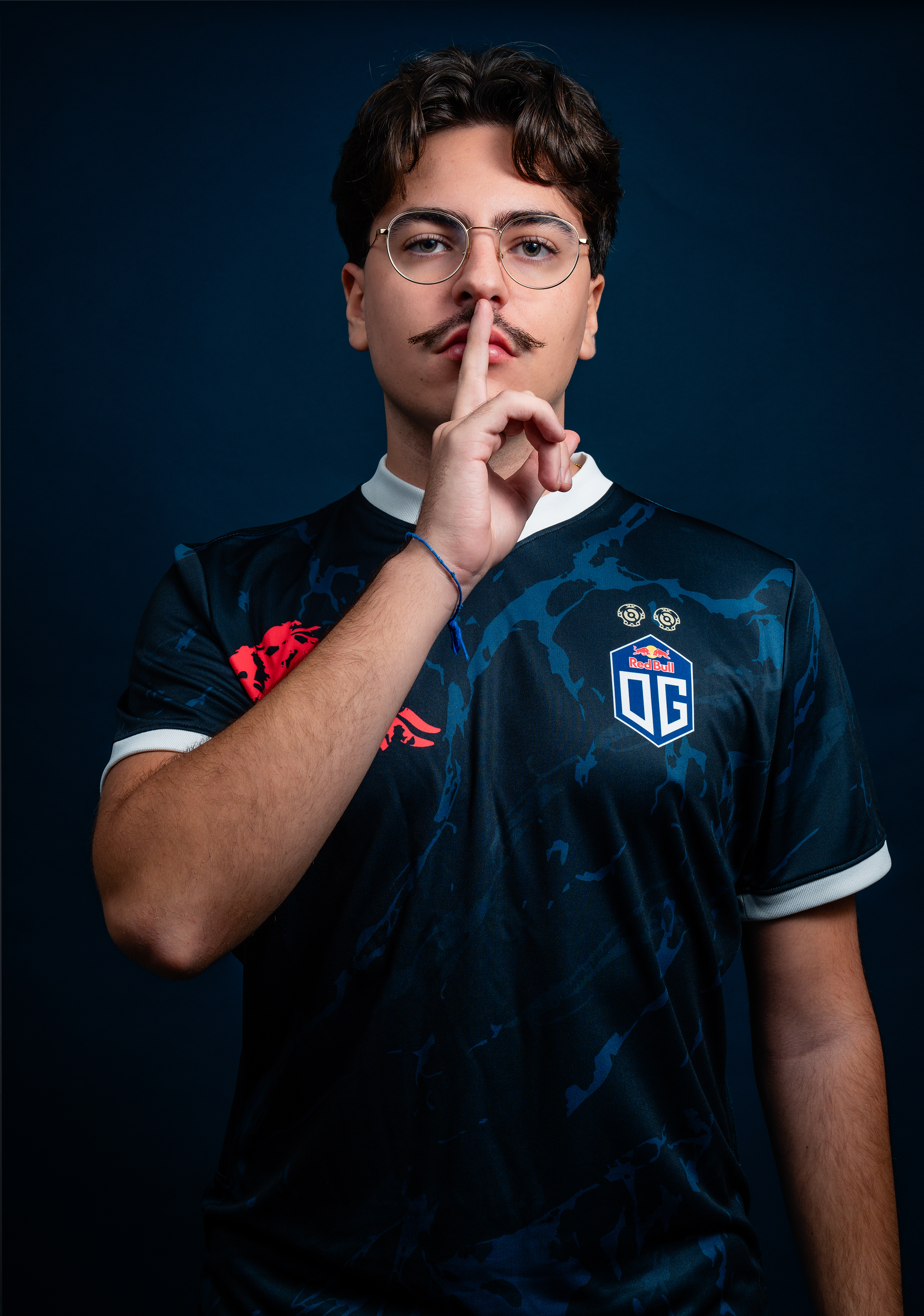 A male model wearing the OG jersey with the OG logo on the left side and a bull logo on the right side, featuring white highlights around the neck and sleeves. The jersey also includes two golden DOTA 2 Aegis symbols above the OG logo.