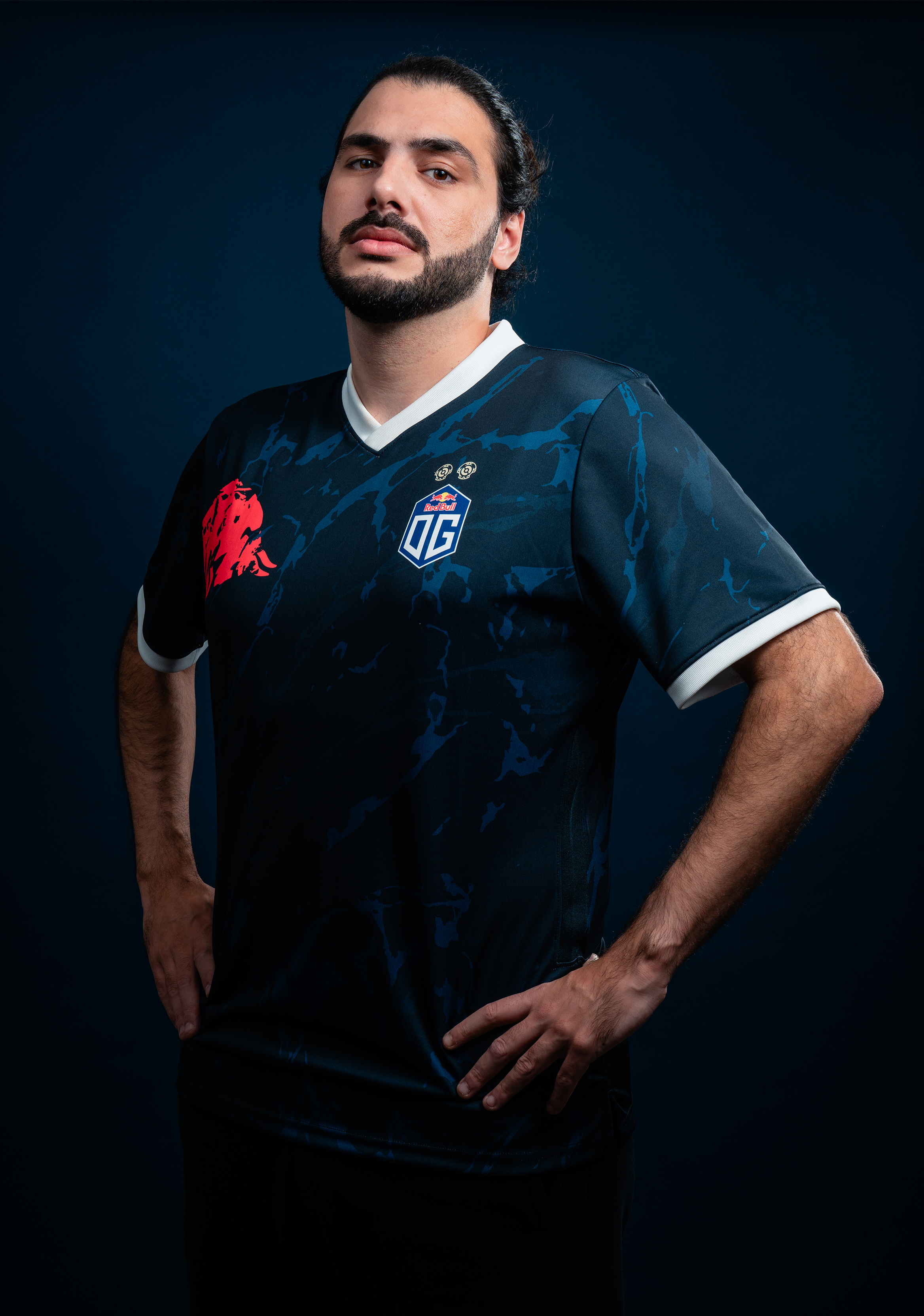 A male model wearing the OG jersey with the OG logo on the left side and a bull logo on the right side, featuring white highlights around the neck and sleeves. The jersey also includes two golden DOTA 2 Aegis symbols above the OG logo.
