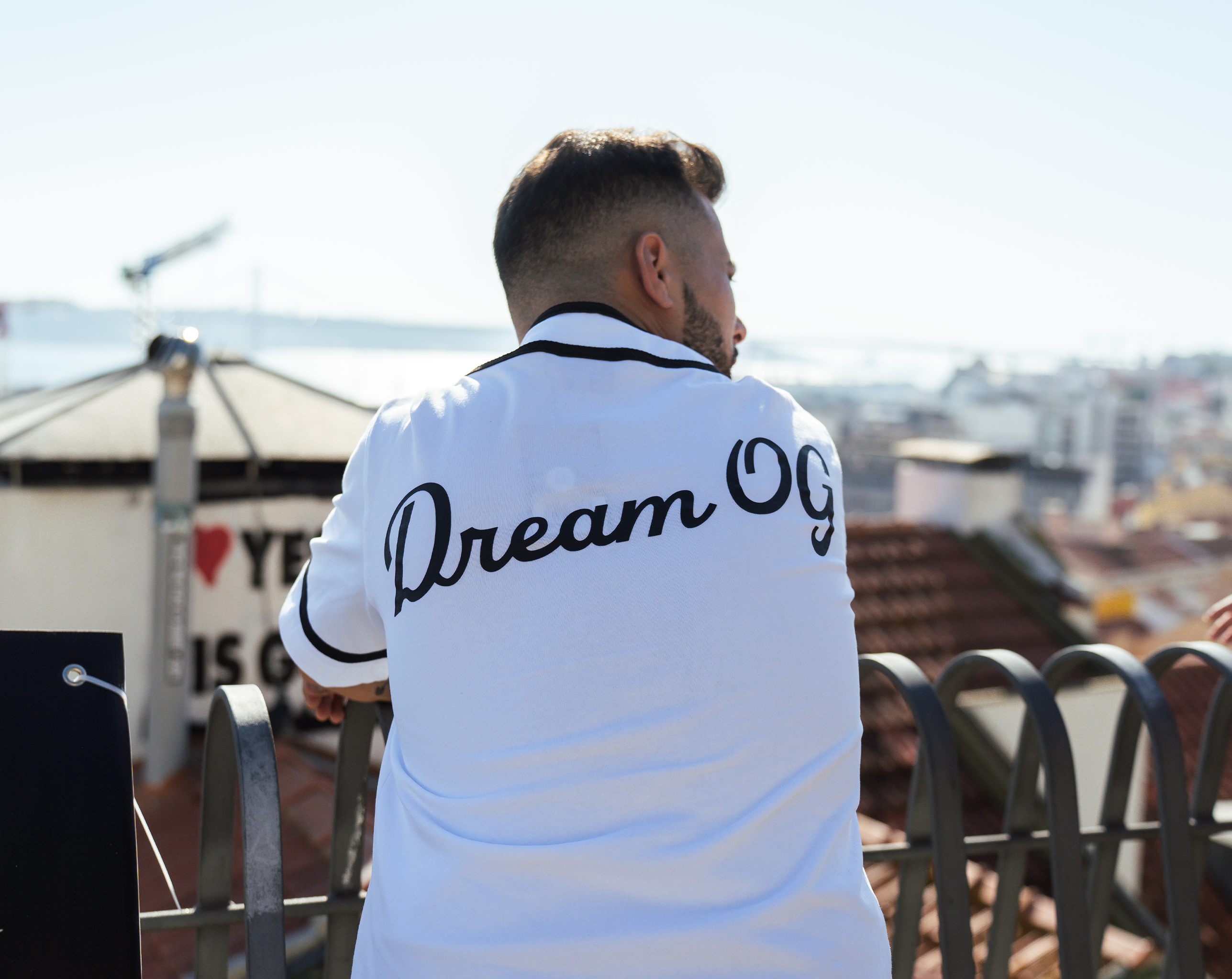 A model posing against a plain background wearing a black and white baseball tee with 'DreamOG' slogan on the backside, showcasing its casual and sporty design.