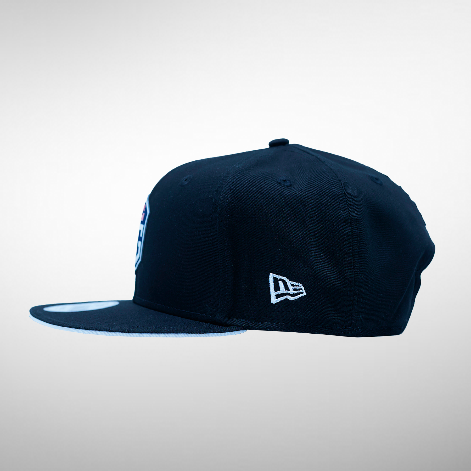 Side view of a dark blue snapback cap, showcasing the OG logo on the front and the New Era logo on the side.