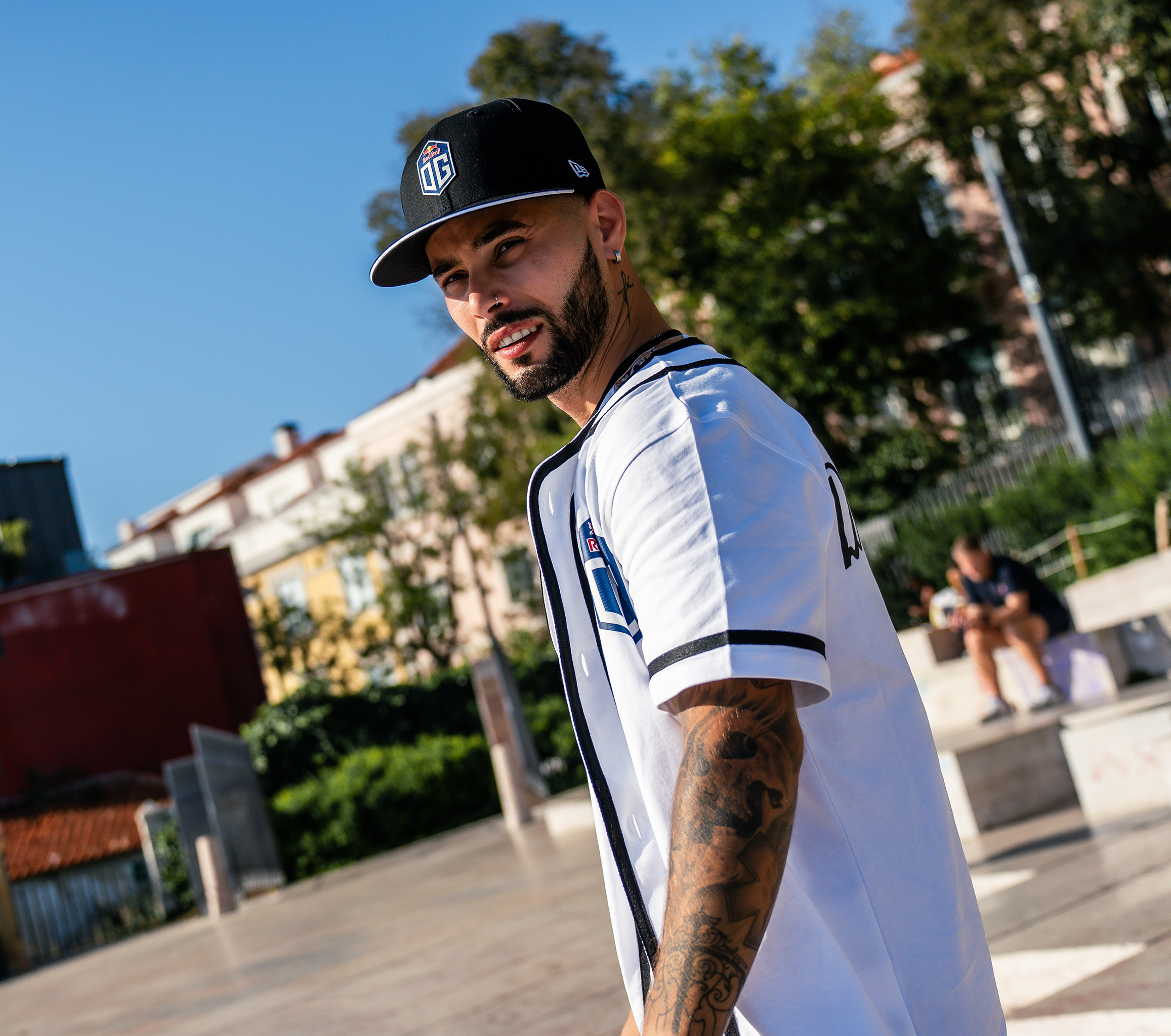 A model wearing a black and white baseball tee with OG logo on the front, posing against a plain background to showcase the casual and sporty design of the shirt.