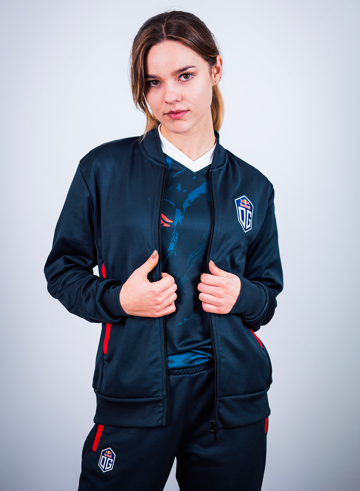 A female model wearing dark blue pro jacket and pants prominently featuring the OG logo.