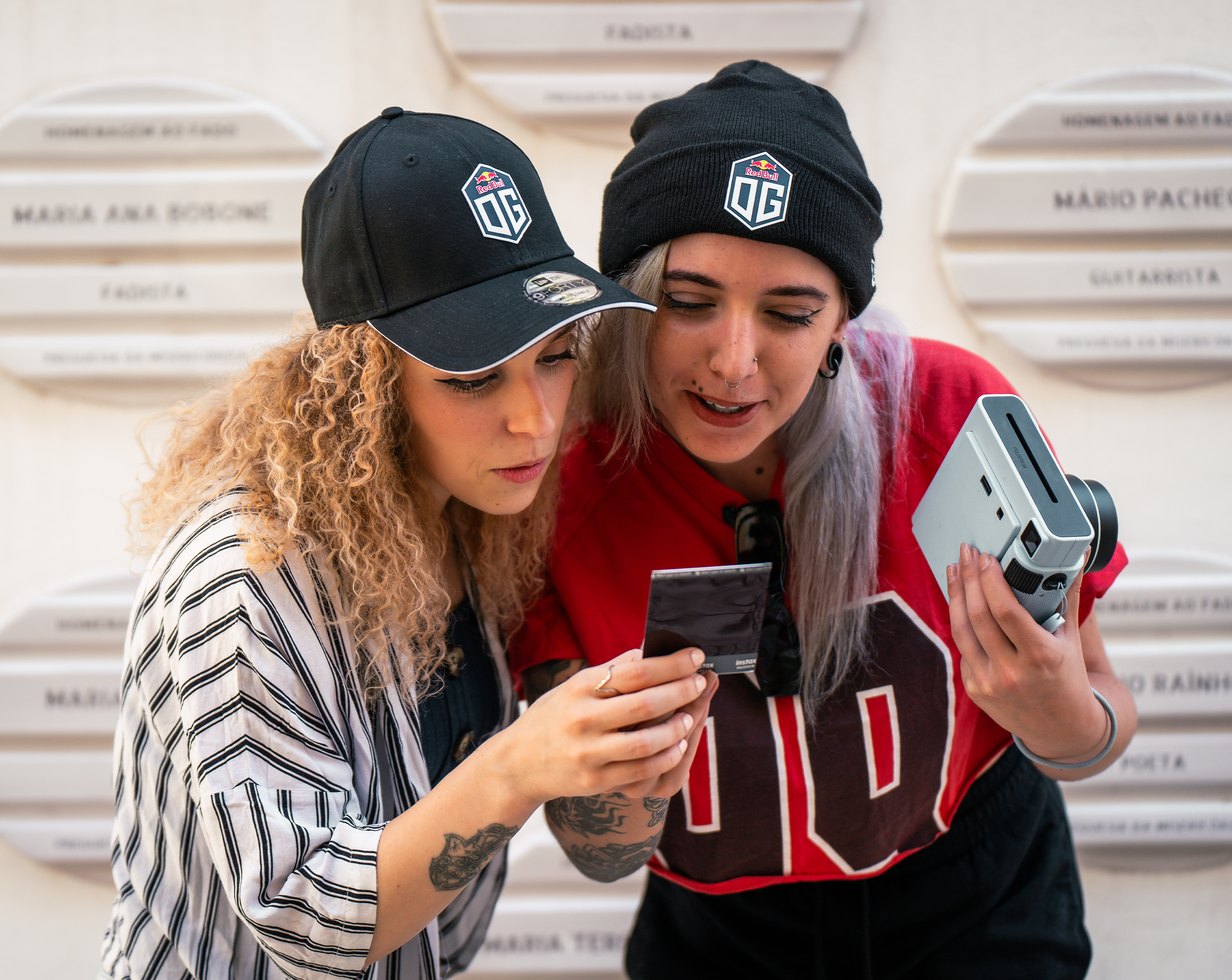 Two female models posing together: one wearing a dark blue cap with the OG logo and New Era logo, and the other wearing a dark blue beanie featuring the OG logo.